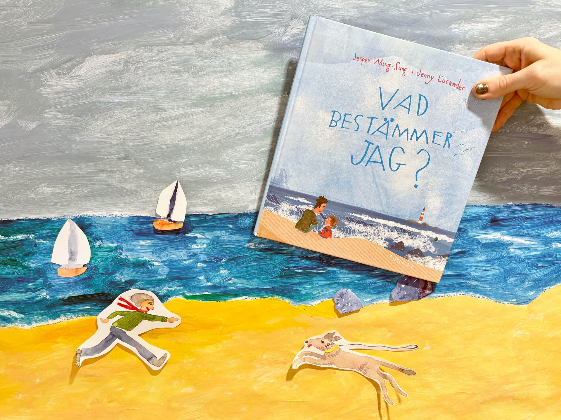 Bilderboken "Vad bestämmer jag?" mot målad bakgrund av strand och hav