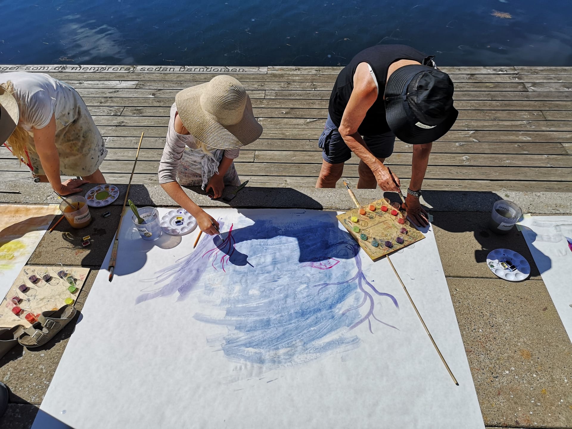 Vuxna målar i solen på bryggan, sett uppifrån