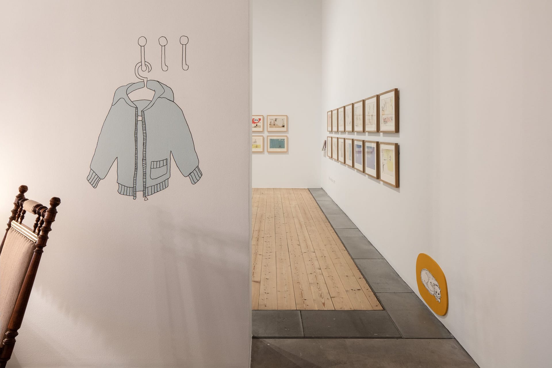Image from the 2018 exhibition, with a painted blue jacket on the wall and framed pictures in the background,