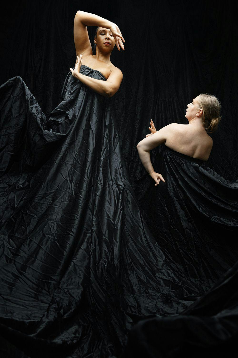 Två dansare i svarta, draperade tyger mot svart tydbakgrund