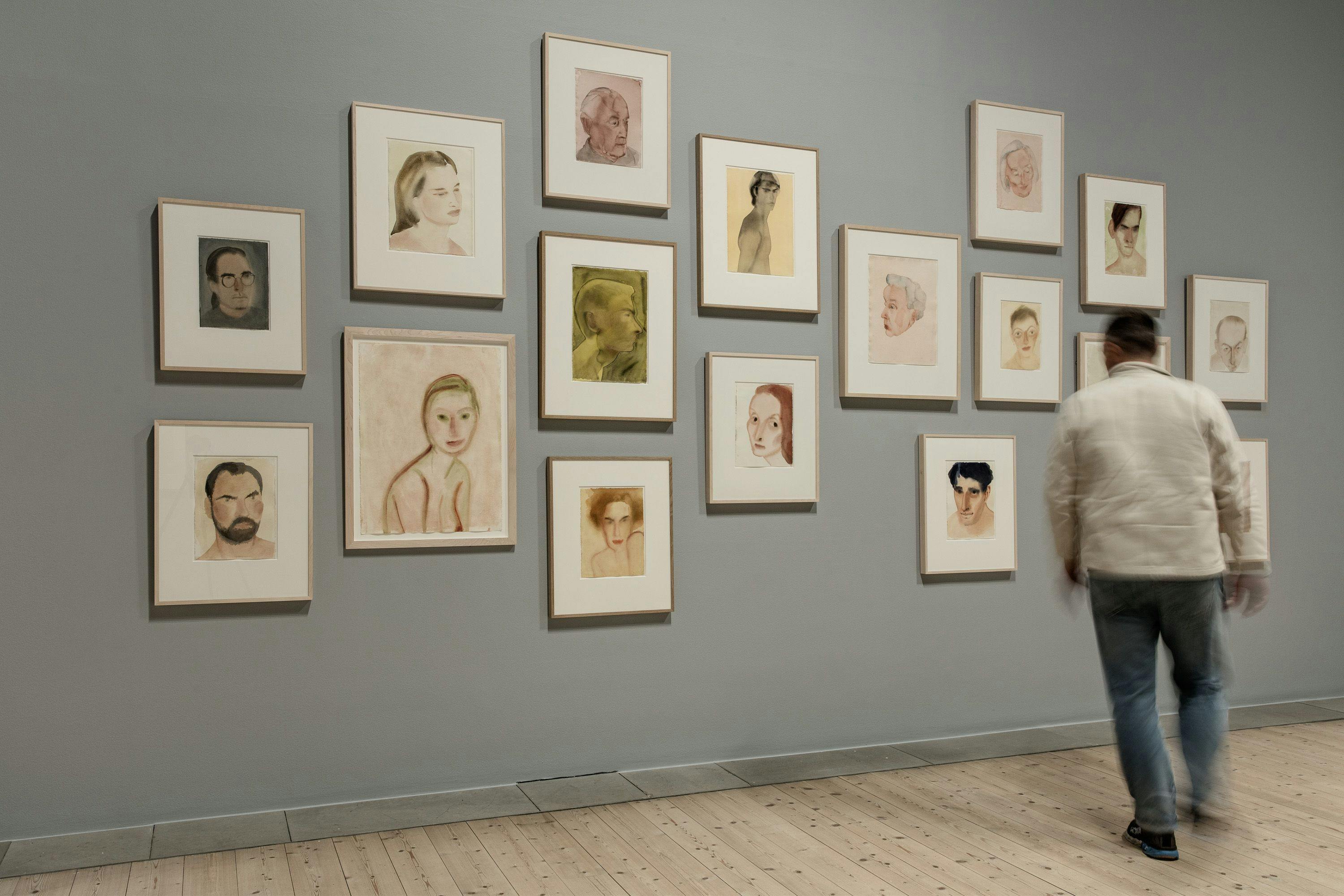 Person walking in front of paintings on a wall by Mats Gustafsson
