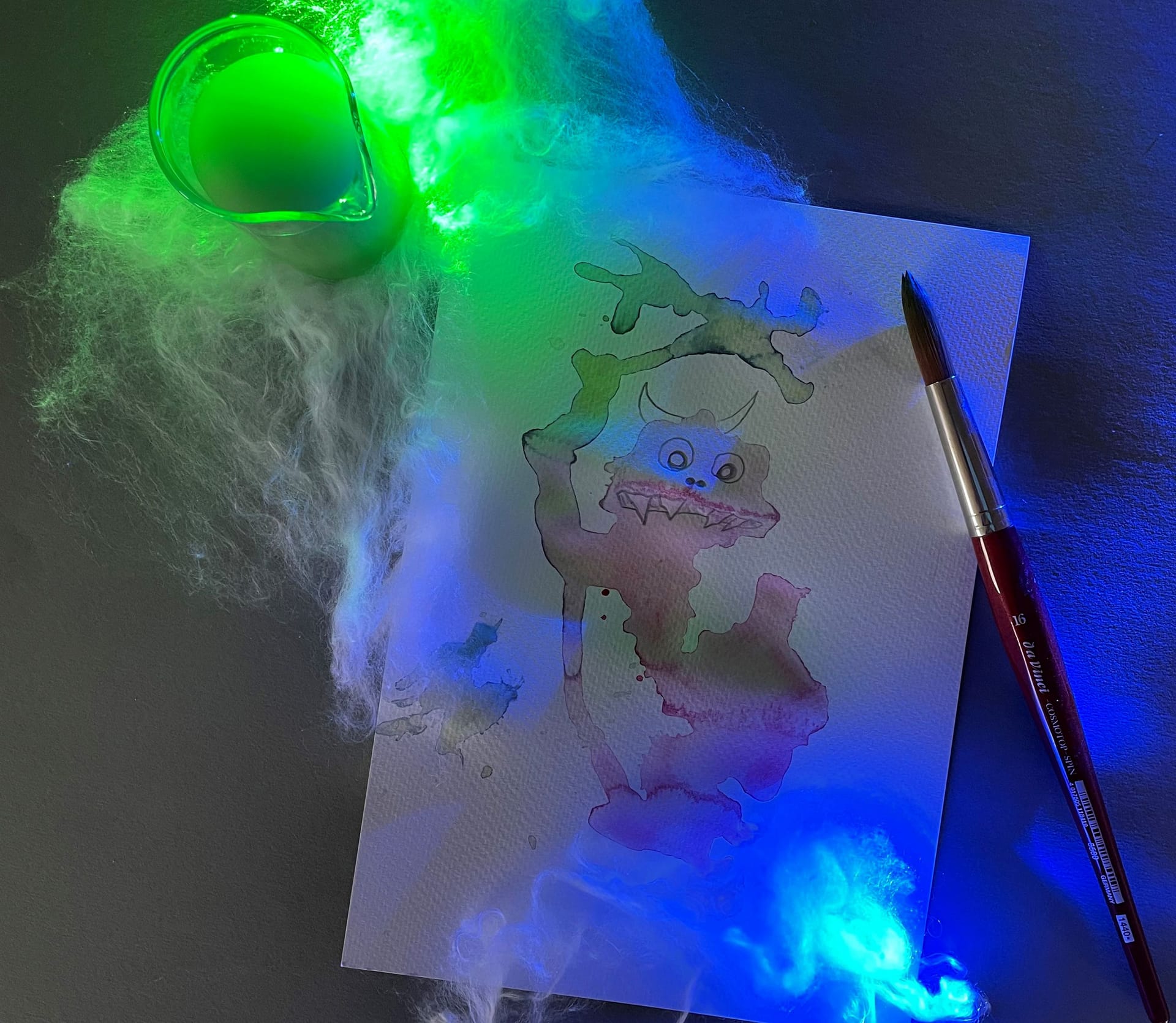 Green and blue lights shine over a watercolour paper with a spot that looks like a monster