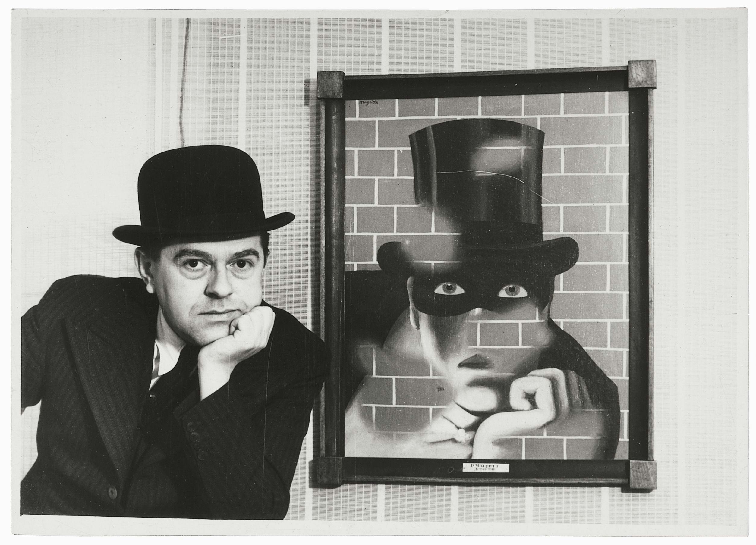 Konstnären Magritte tittar in i kameran bredvid en tavla