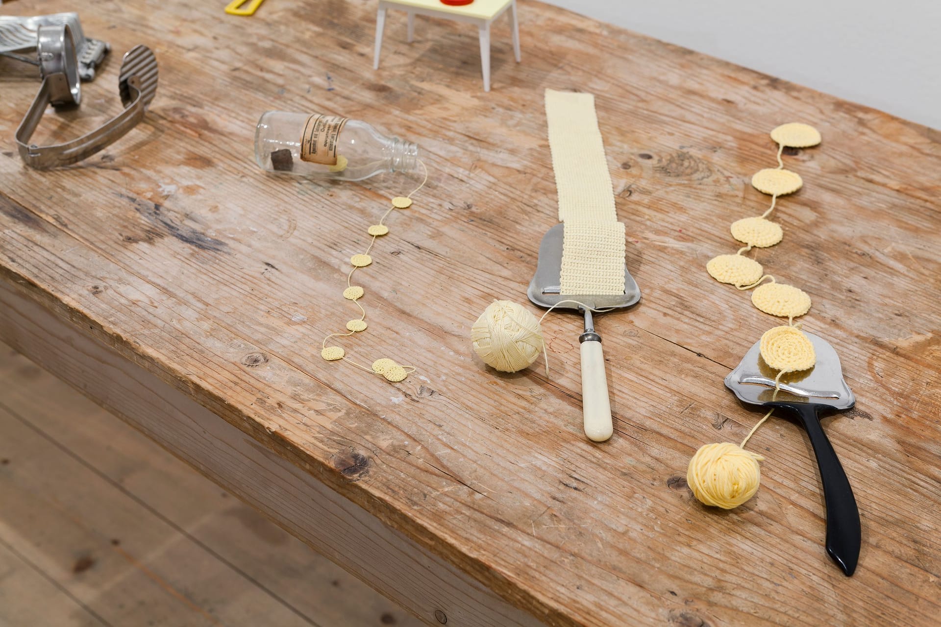 Artwork on a wooden table, consisting of yellow yarn and cheese slicers.