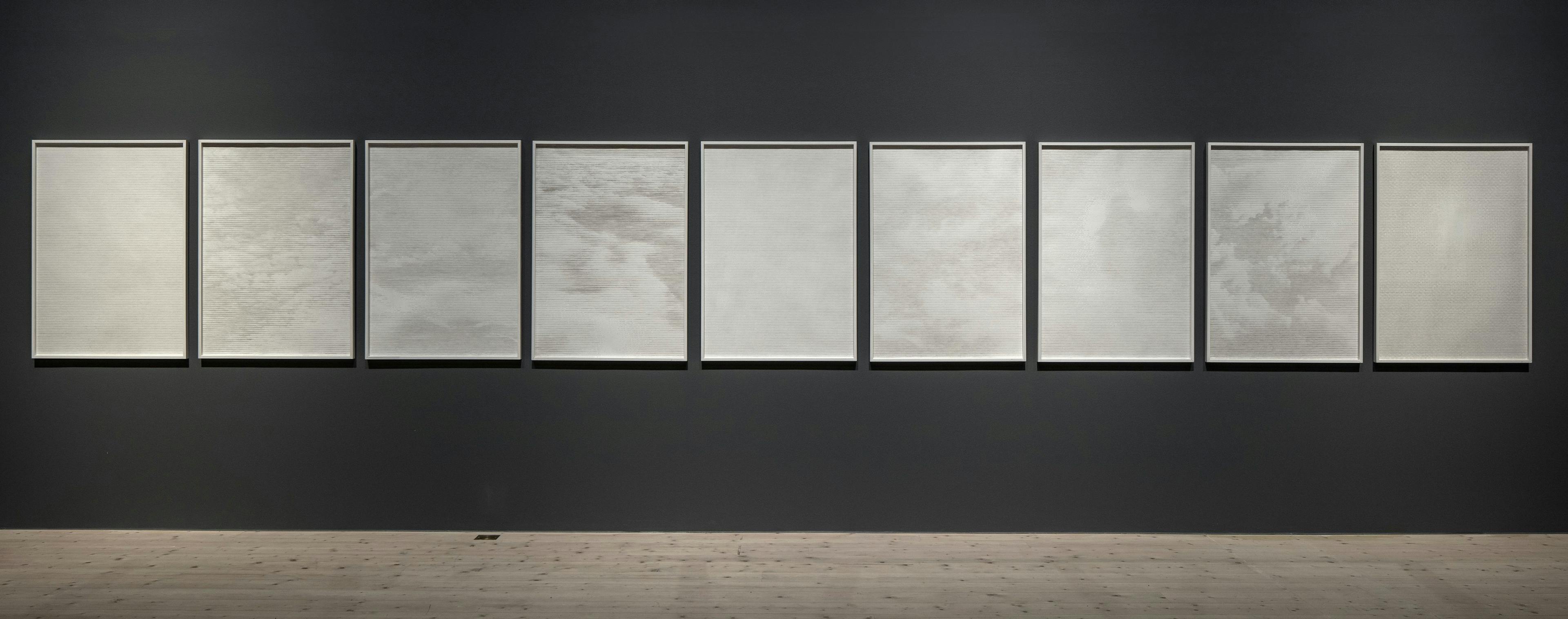 Åtta verk ur serien Oceaner av luft (av Anna Ling 2010) hänger på en mörkgrå vägg