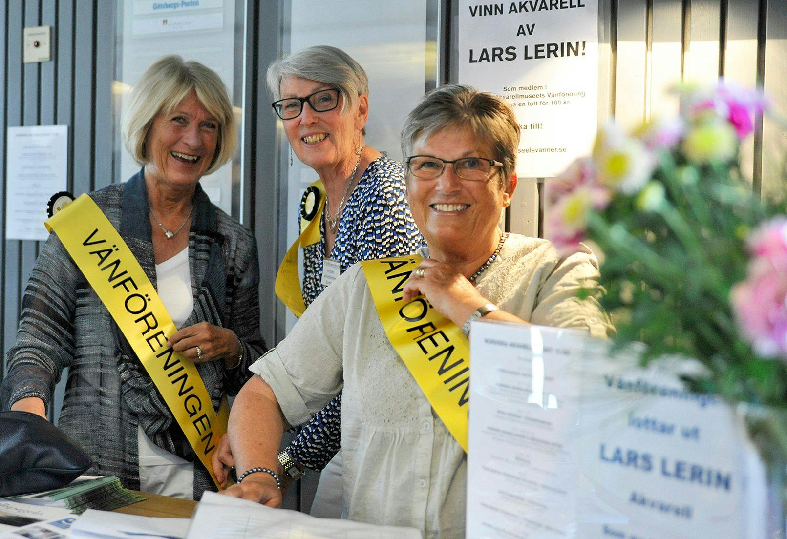 Tre glada personer med gula band med texten "Vänföreningen"