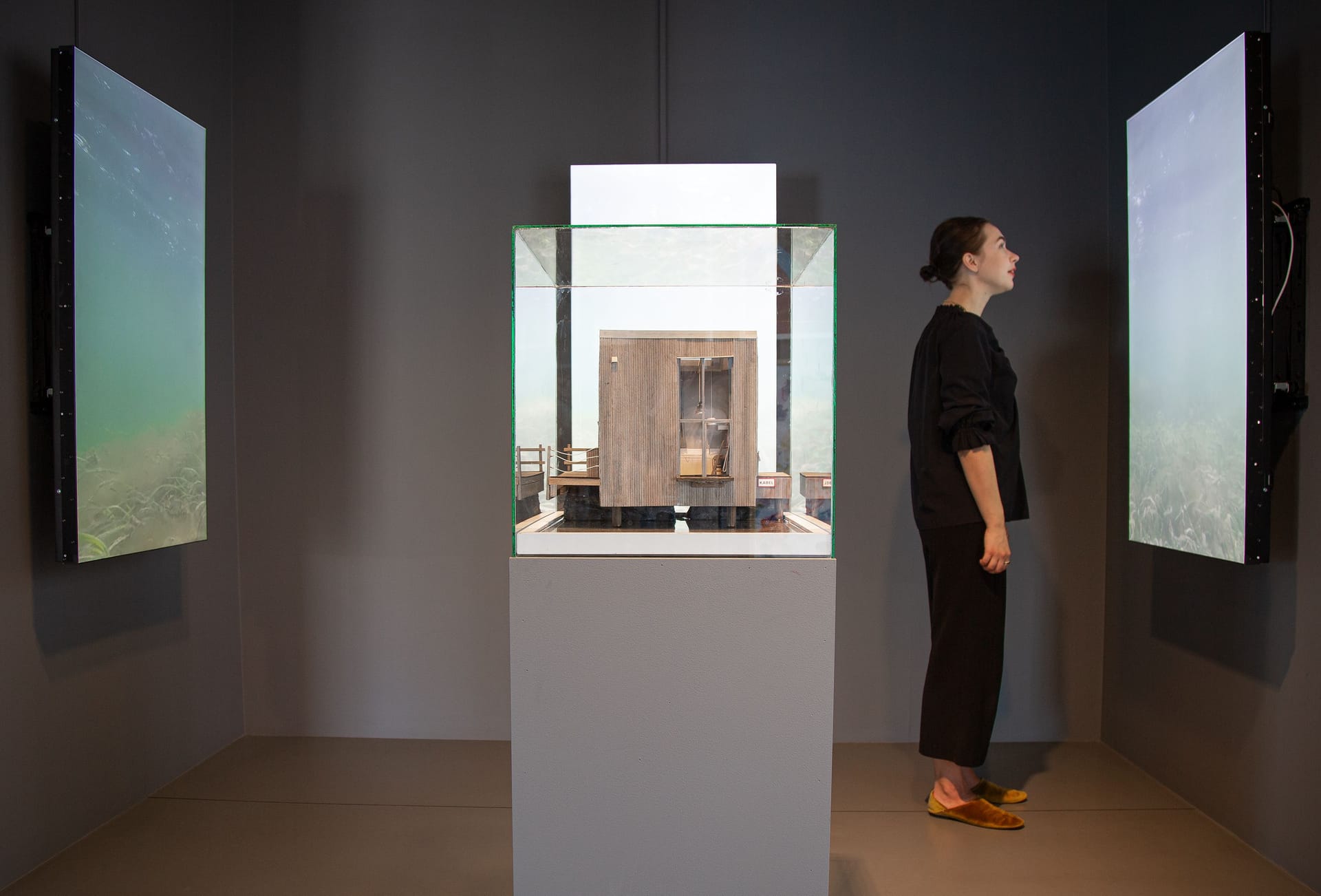 Person tittar på skärm brevid miniatyrbyggnad i monter