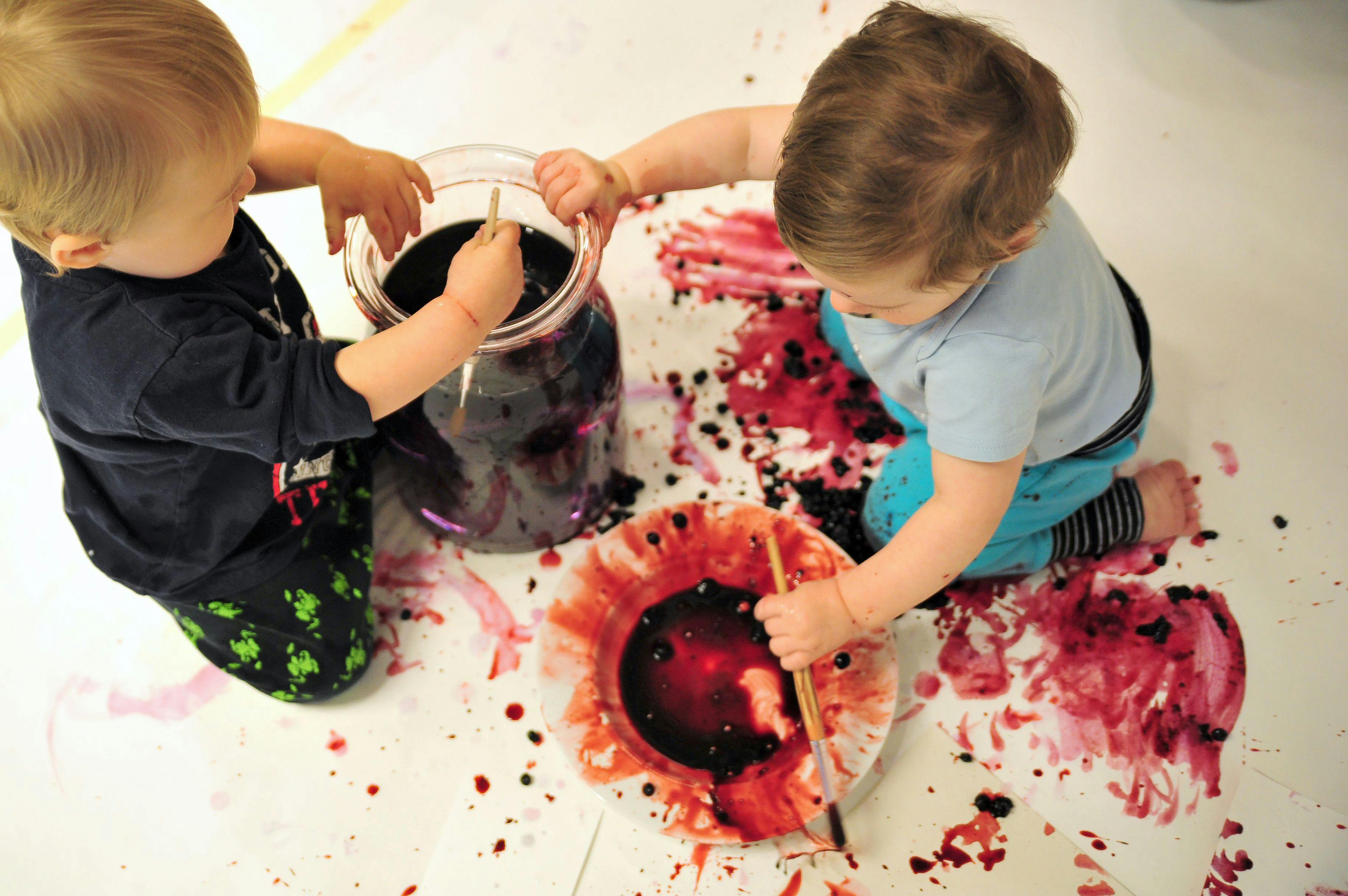 Two babies painting with blueberries and water on a big piece of paper