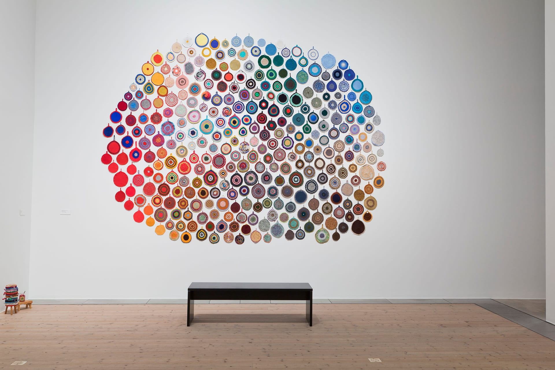 Work by Anu Tuominen on a white wall, consisting of potholders in different colors arranged in a large circle