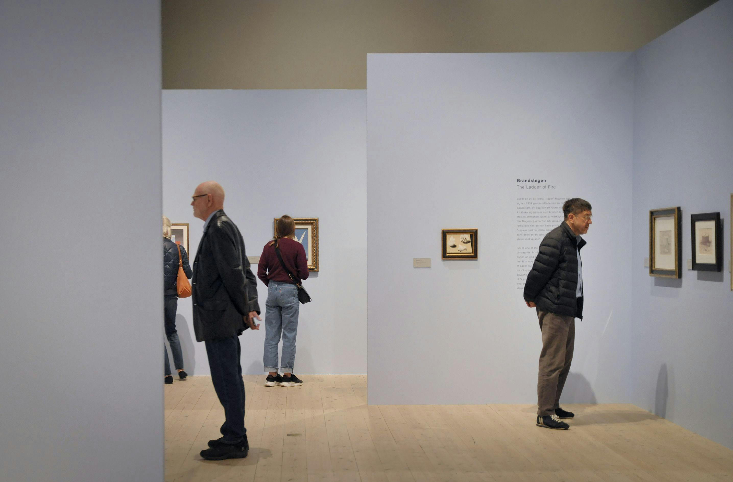 Besökare tittar på konst av Magritte på violetta väggar