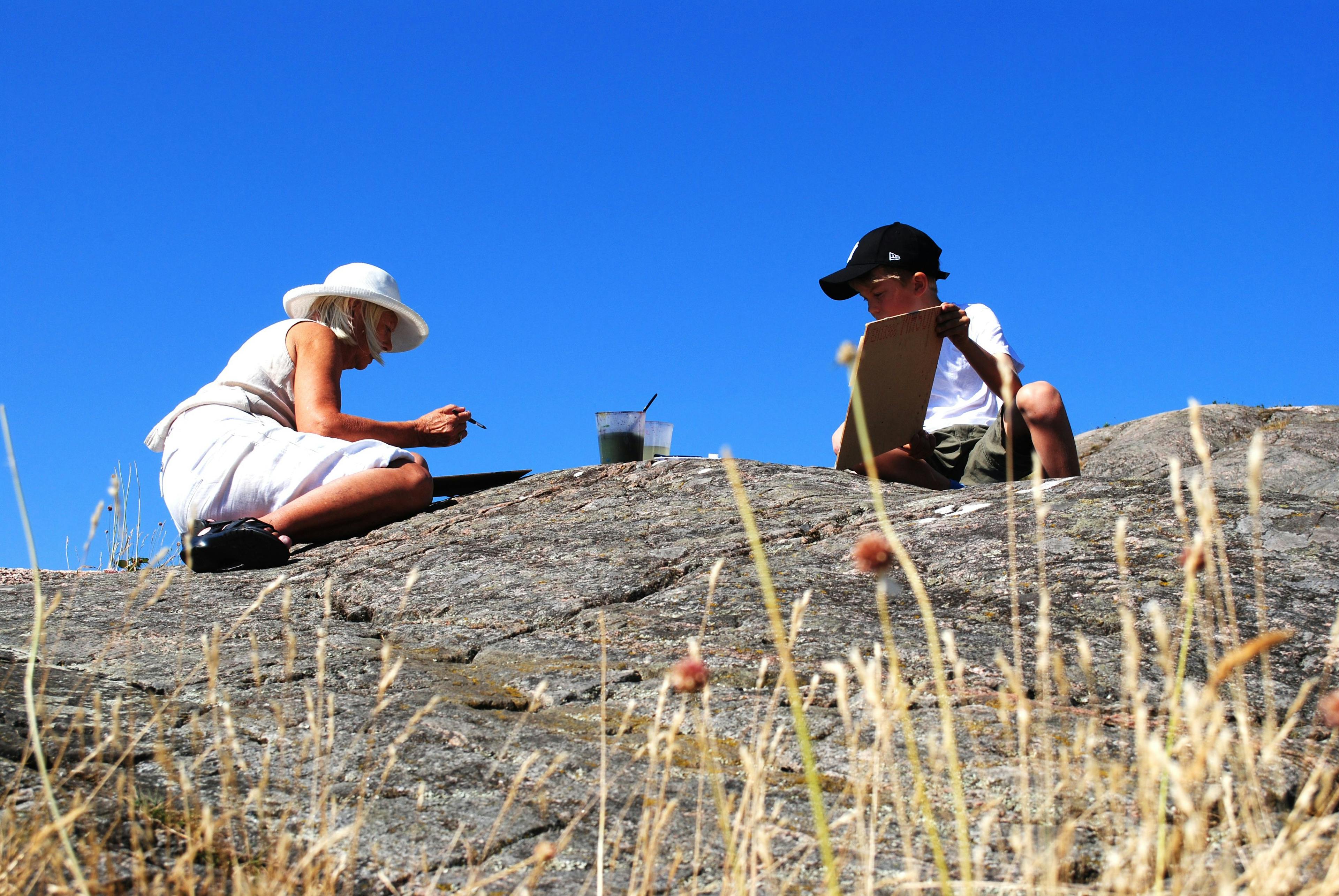 Vuxen och barn sitter och målar på en klippa