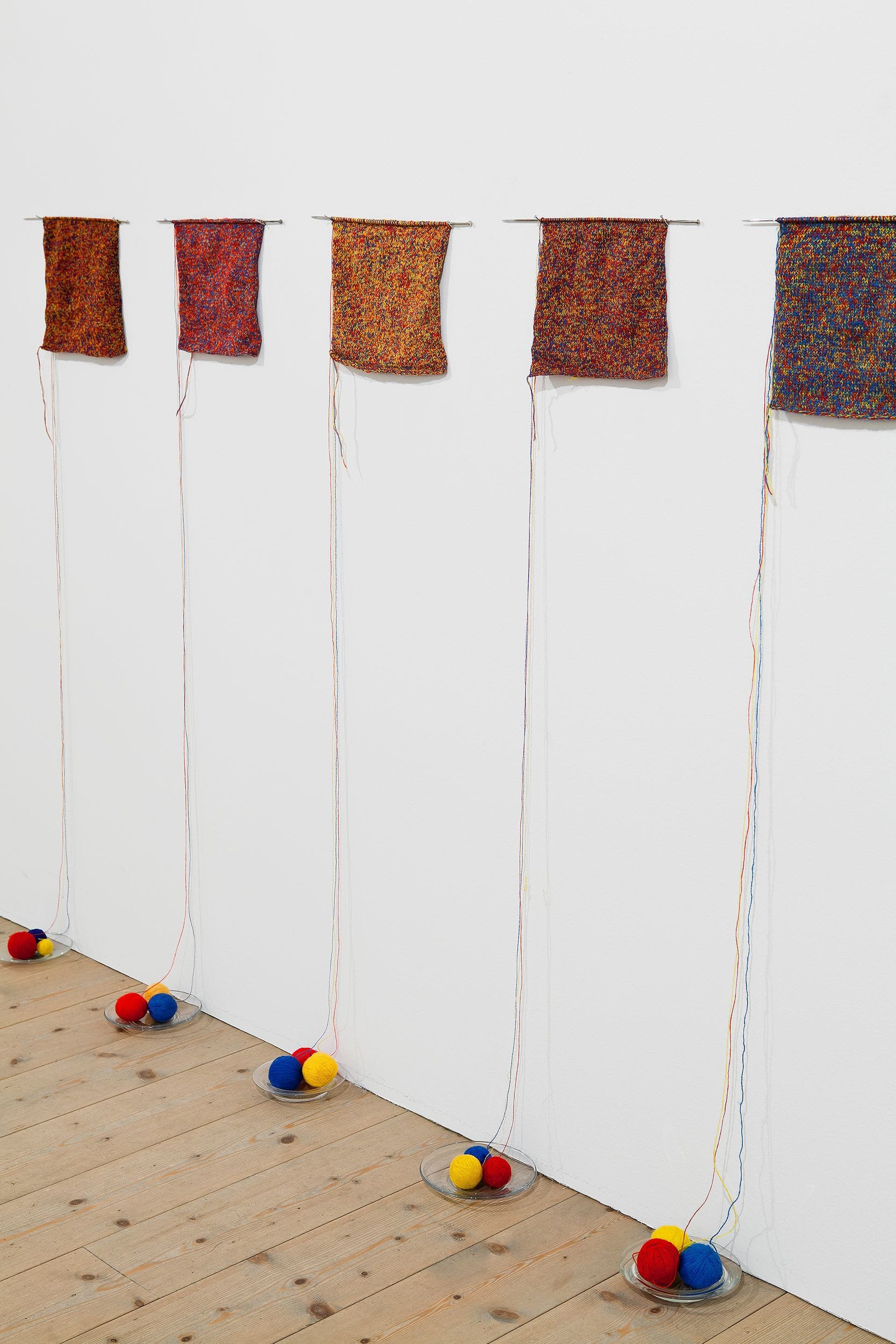 Artwork made of yarn and yarn balls by Anu Tuominen against a white wall.