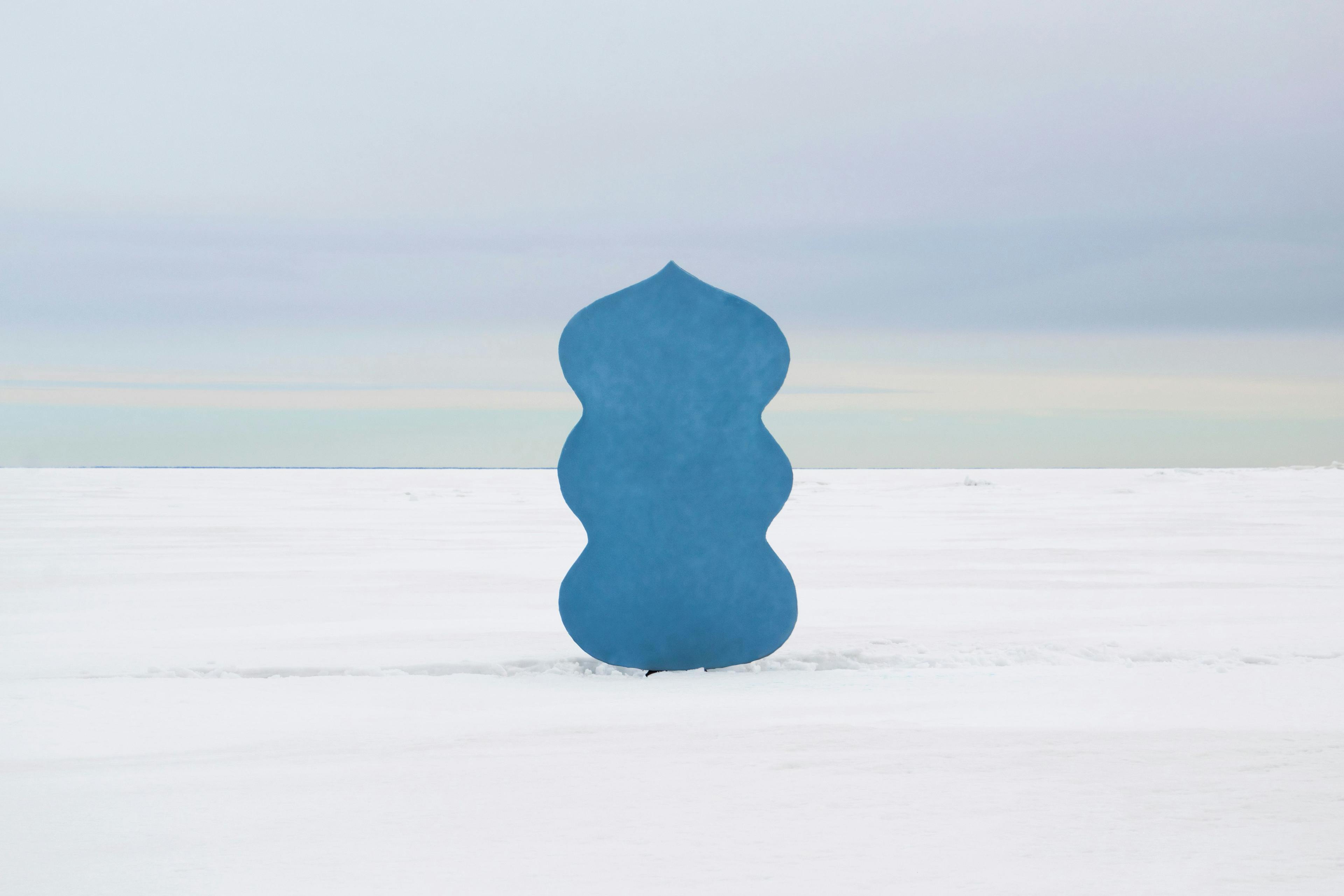 En blå skulptur i platt snölandskap
