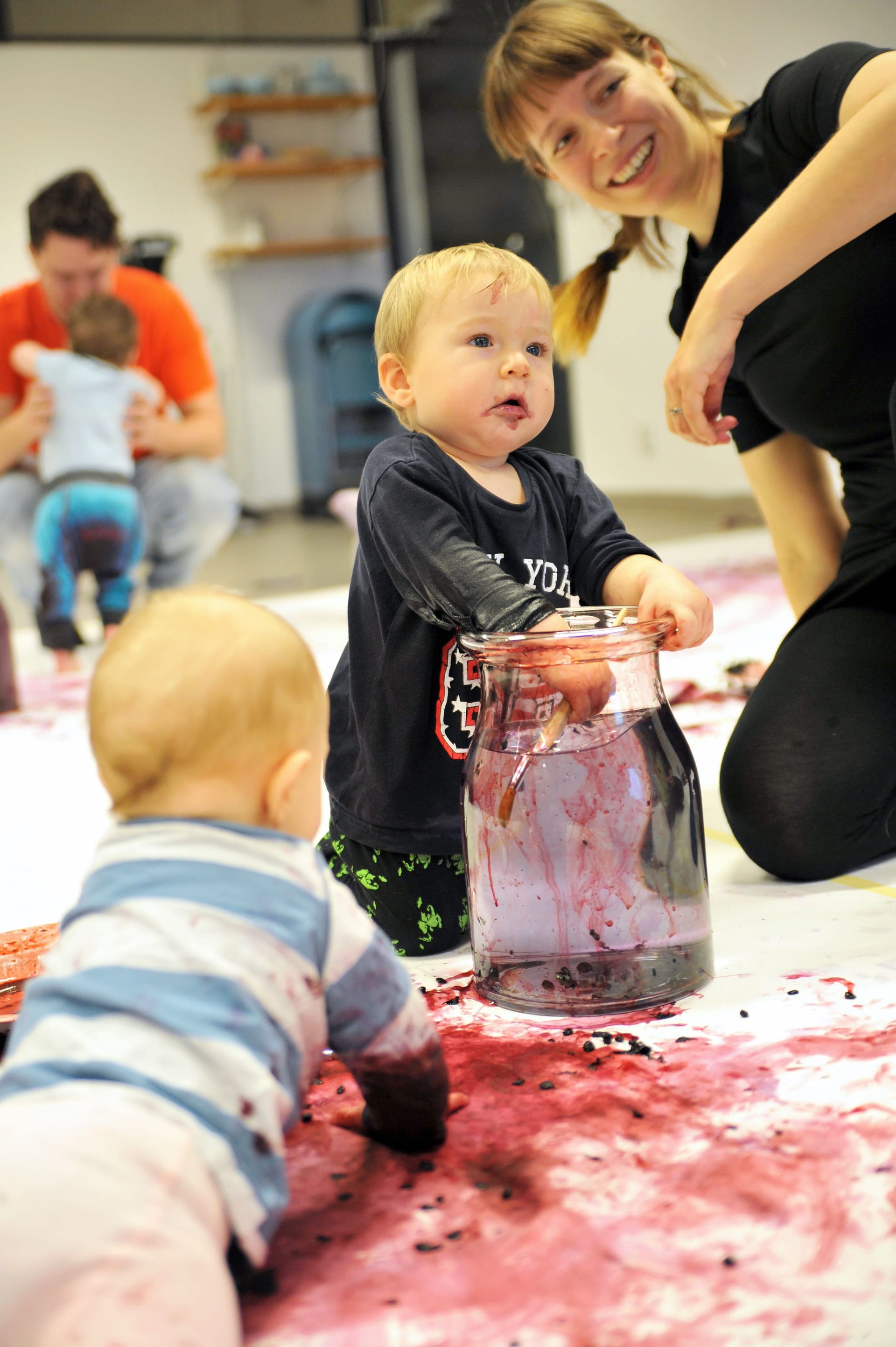 Babies playing with blueberries and a laughing parent