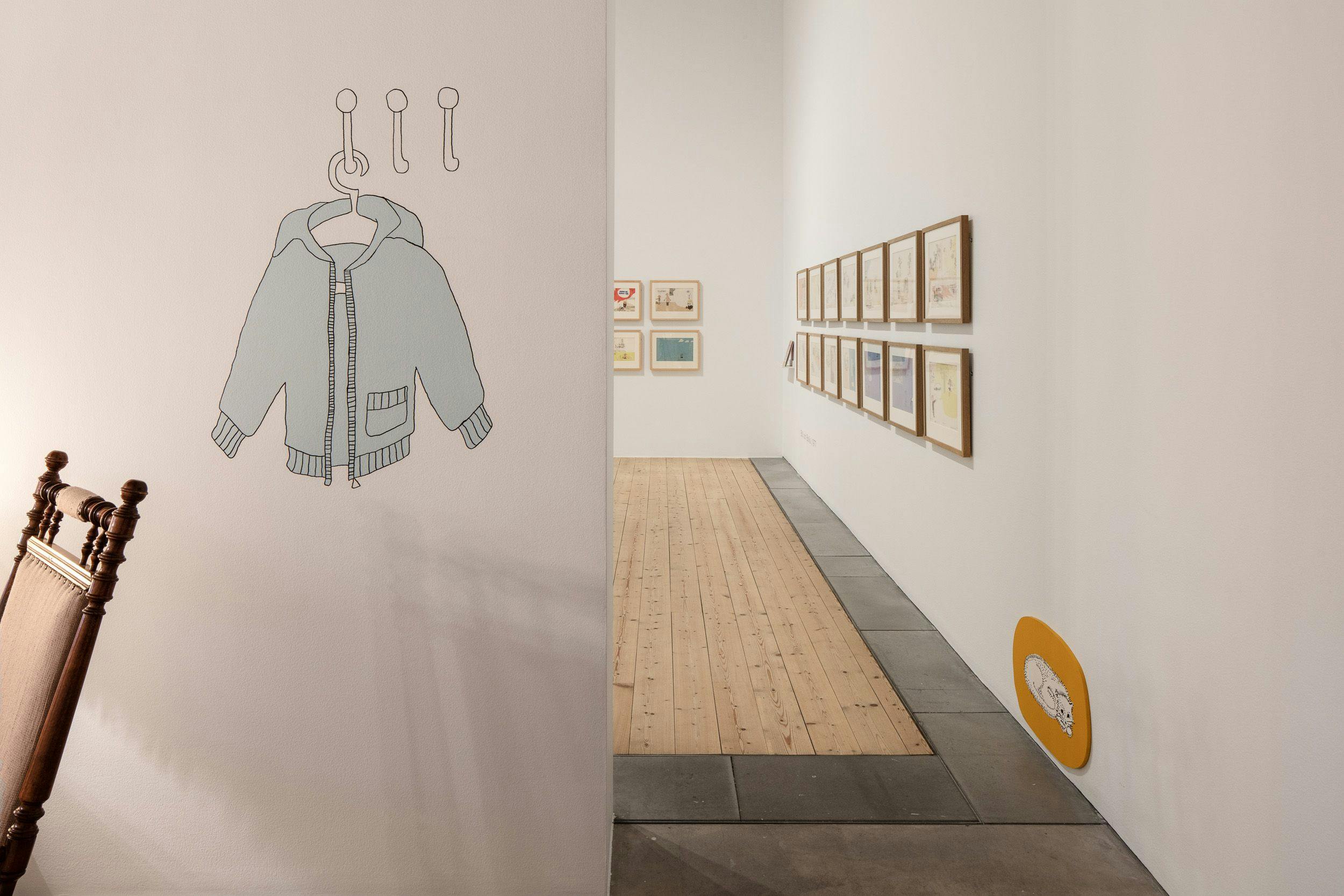 Bild från utställningen 2018, med en målad blå jacka på väggen och tavlor i bakgrunden,