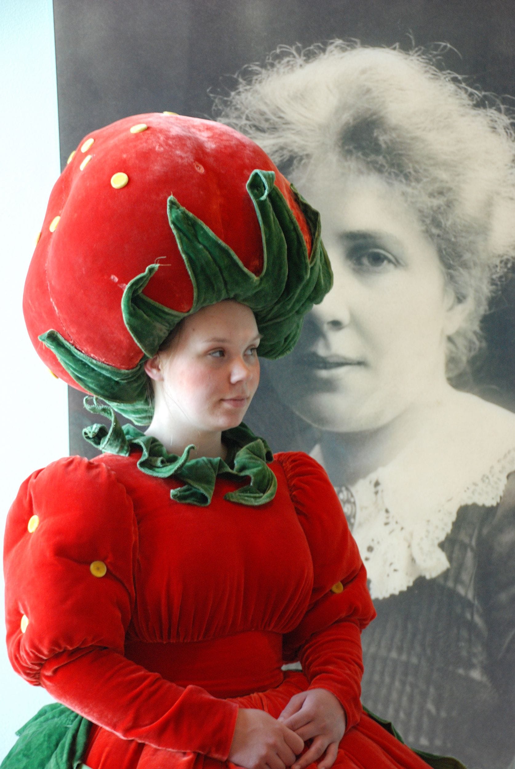 Someone dressed as a strawberry for the exhibition opening, in front of a portrait with Beskow
