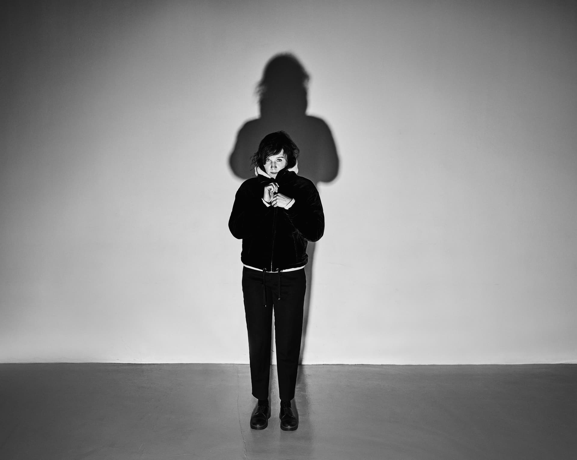 Iiris Viljanen i svartvitt, mörkklädd mot ljus bakgrund med skarpa skuggor